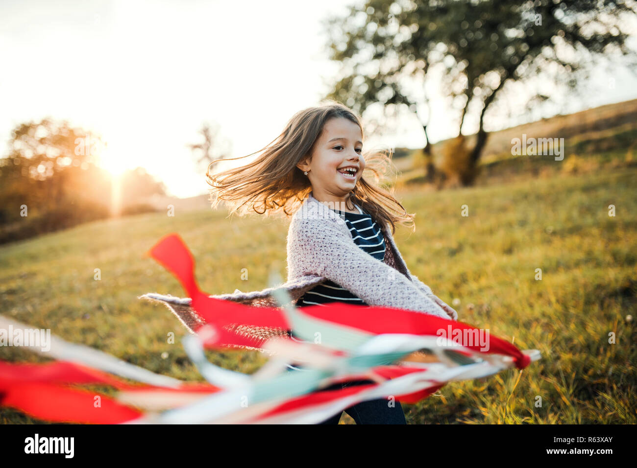 Eine kleine Mädchen spielen mit einem Regenbogen hand Kite im Herbst Natur bei Sonnenuntergang. Stockfoto