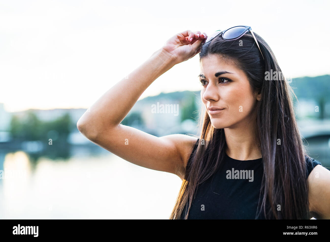 Schöne Frau in schwarzem Kleid auf einem Fluss in der Stadt Prag, Sonnenbrille Holding. Stockfoto