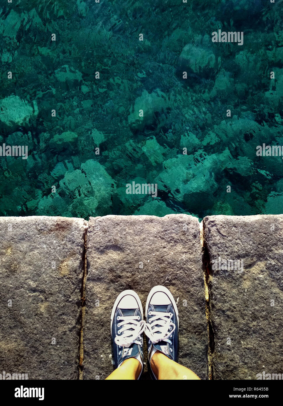 Dies ist eine Ansicht von oben ein Mädchen tragen Converse canvas Schuhe  mit nackten Beinen gegen den klaren grünen Meer Wasser in Sizilien, Italien  Stockfotografie - Alamy