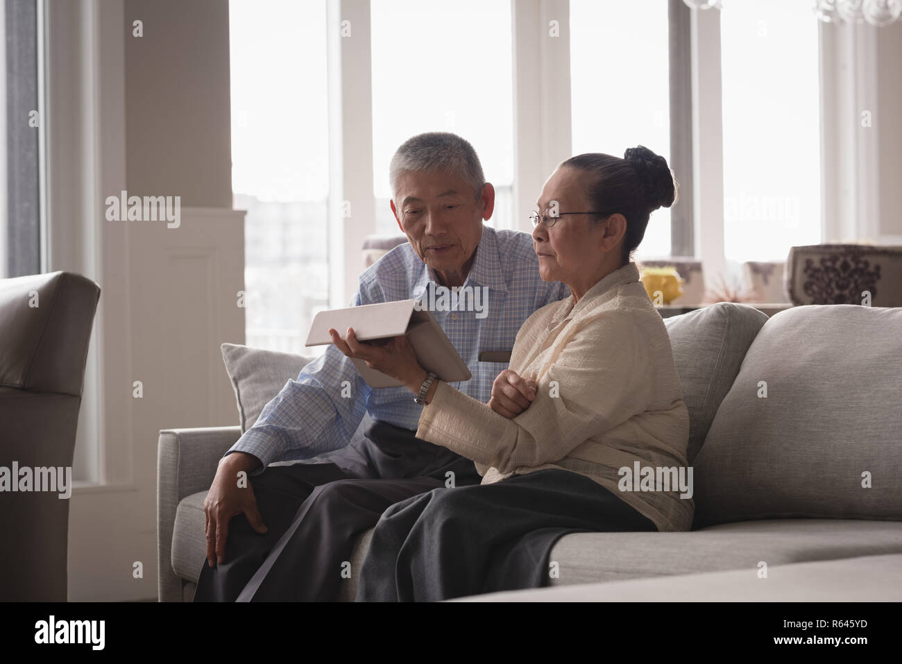 Senior Paar diskutieren über eine digitale Tablet auf dem Sofa im Wohnzimmer. Stockfoto