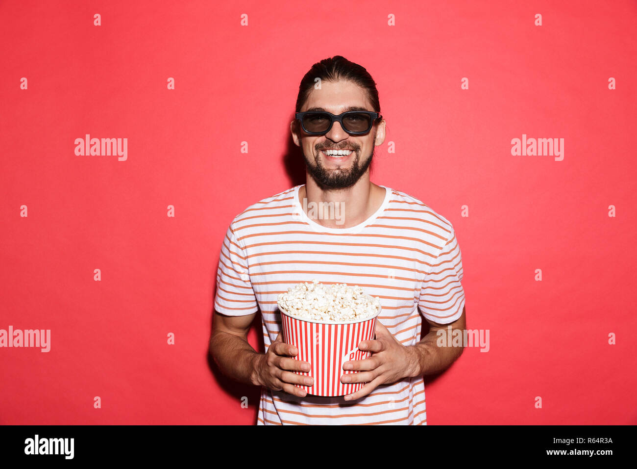 Portrait von Laughing Man in der 3D-Brille aufzupassen Film, essen Popcorn über den roten Hintergrund isoliert Stockfoto