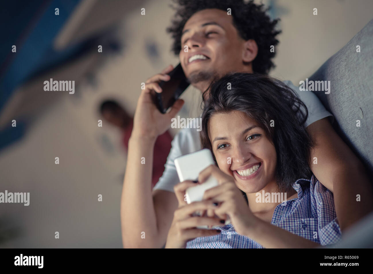 Attraktive Paare sitzen auf der Couch zusammen am Smartphone suchen zu Hause im Wohnzimmer Stockfoto