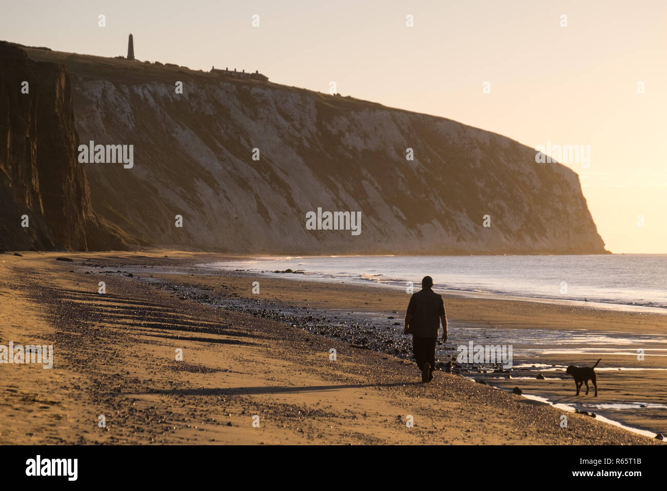 Ein Mann, der seinen Hund bei Sonnenaufgang am Yaverland Strand auf der Isle of Wight, Großbritannien Stockfoto