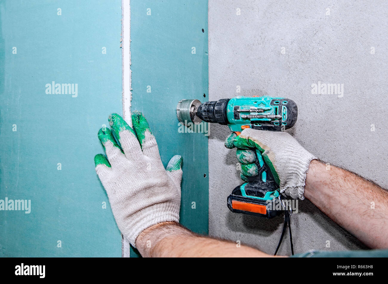 Ein Arbeiter bohrt Löcher in einem gipskartonplatten Wand mit einer elektrischen Bohrmaschine. Reparatur im Haus. Stockfoto