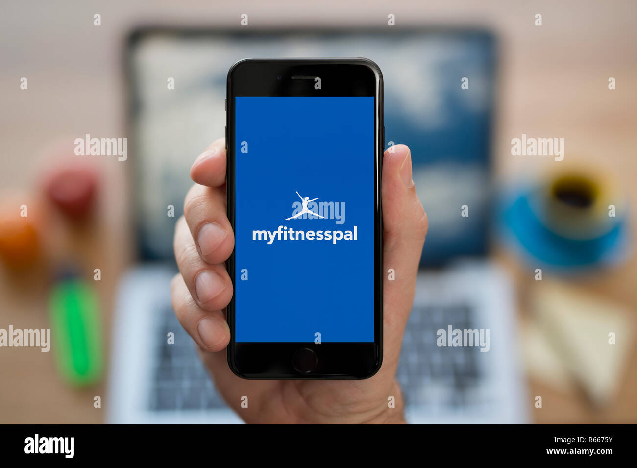 Ein Mann schaut auf seinem iPhone die zeigt die MyFitnessPal logo, während saß an seinem Computer Schreibtisch (nur redaktionelle Nutzung). Stockfoto