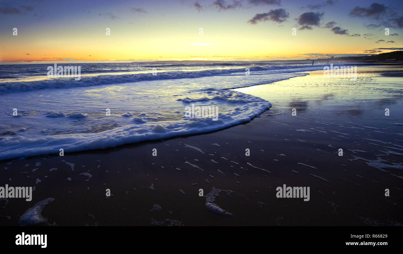 Die Wellen über den Sand am Strand bei Sonnenuntergang mit schönen Himmel Stockfoto