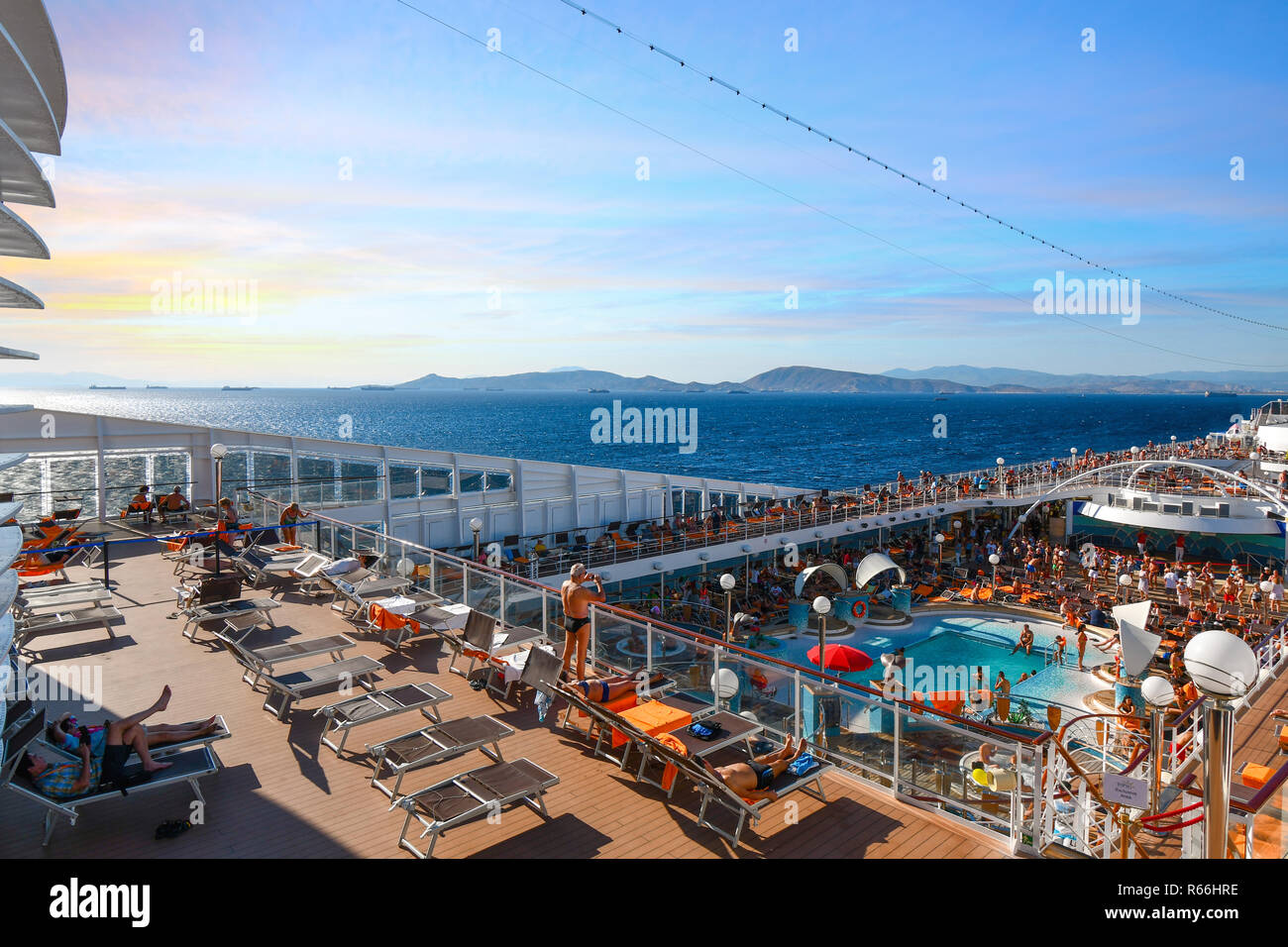Kreuzfahrtschiff Passagiere auf dem oberen Deck eines Schiffes genießen Sie den Pool und die Sonne, wie Sie der Hafen von Piraeus in der Nähe der Küste von Athen Griechenland verlassen Stockfoto
