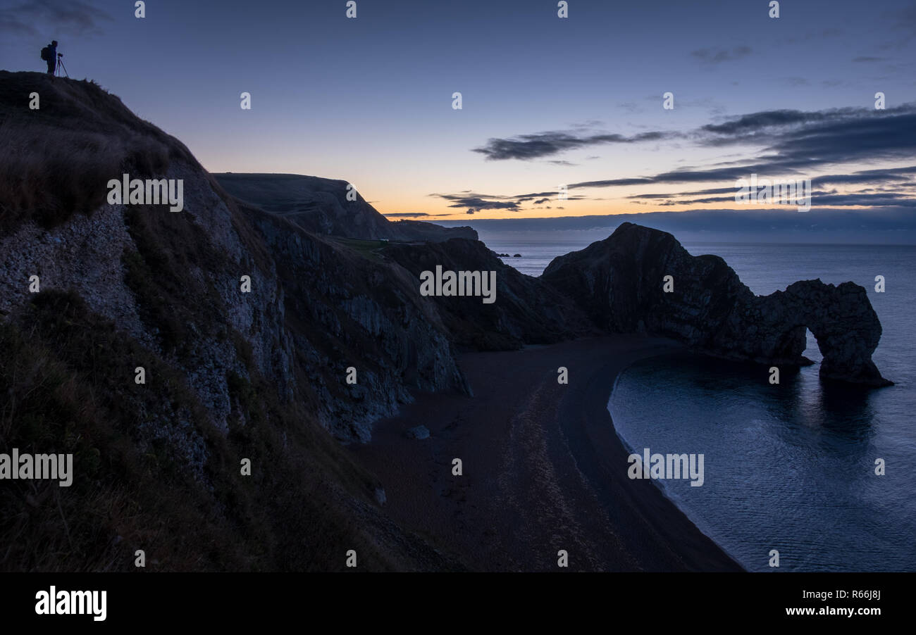 Ein Fotograf seine Kamera vorbereiten für den Sonnenaufgang über Durdle Door auf in Dorset Jurassic Coast Stockfoto