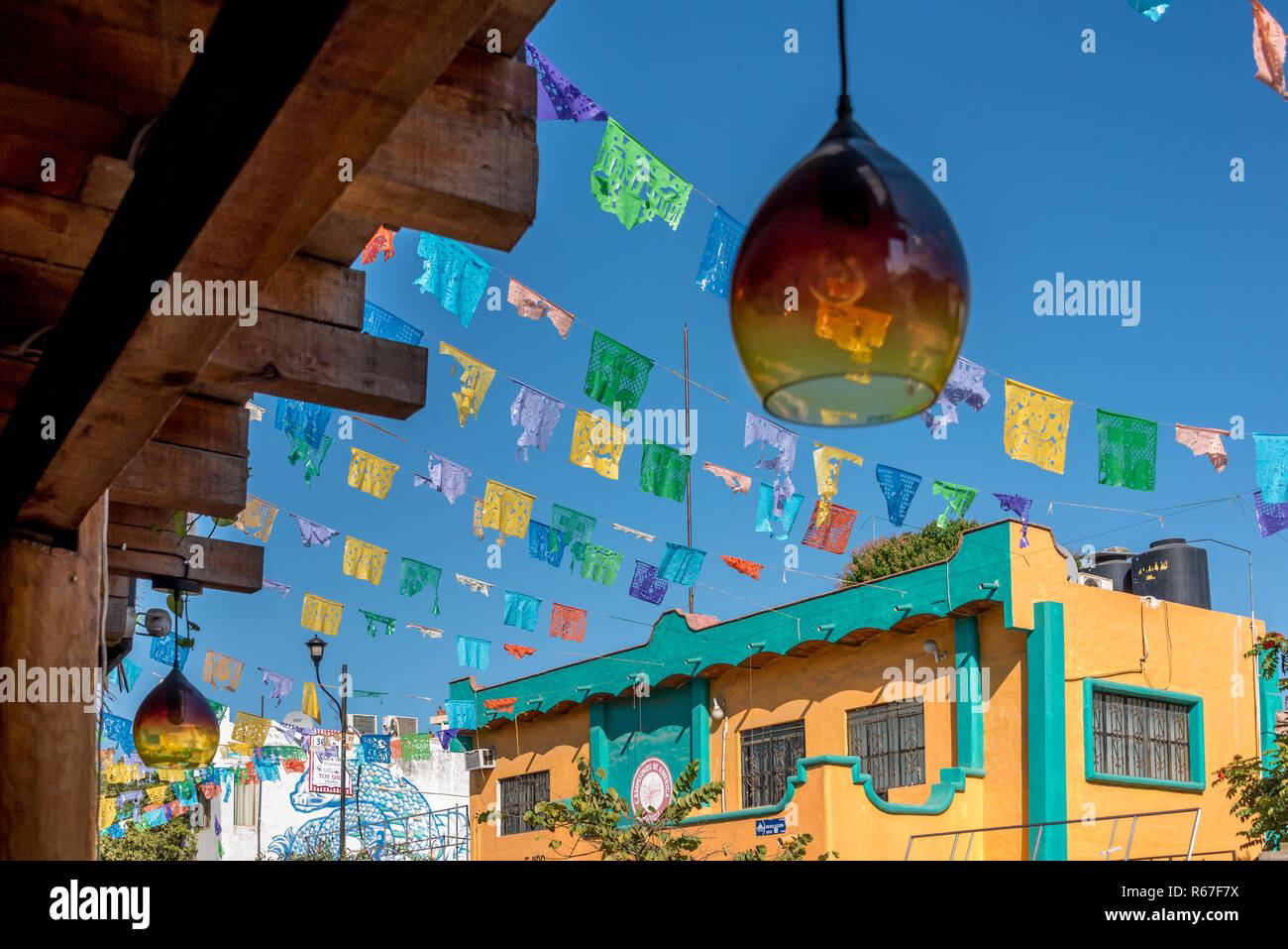 Auf der Suche durch, mundgeblasenem Glas Lampe hängende Outside cafe in Sayulita, Mexiko, mit bunten Papel picado Fahnen auf der anderen Straßenseite. Stockfoto