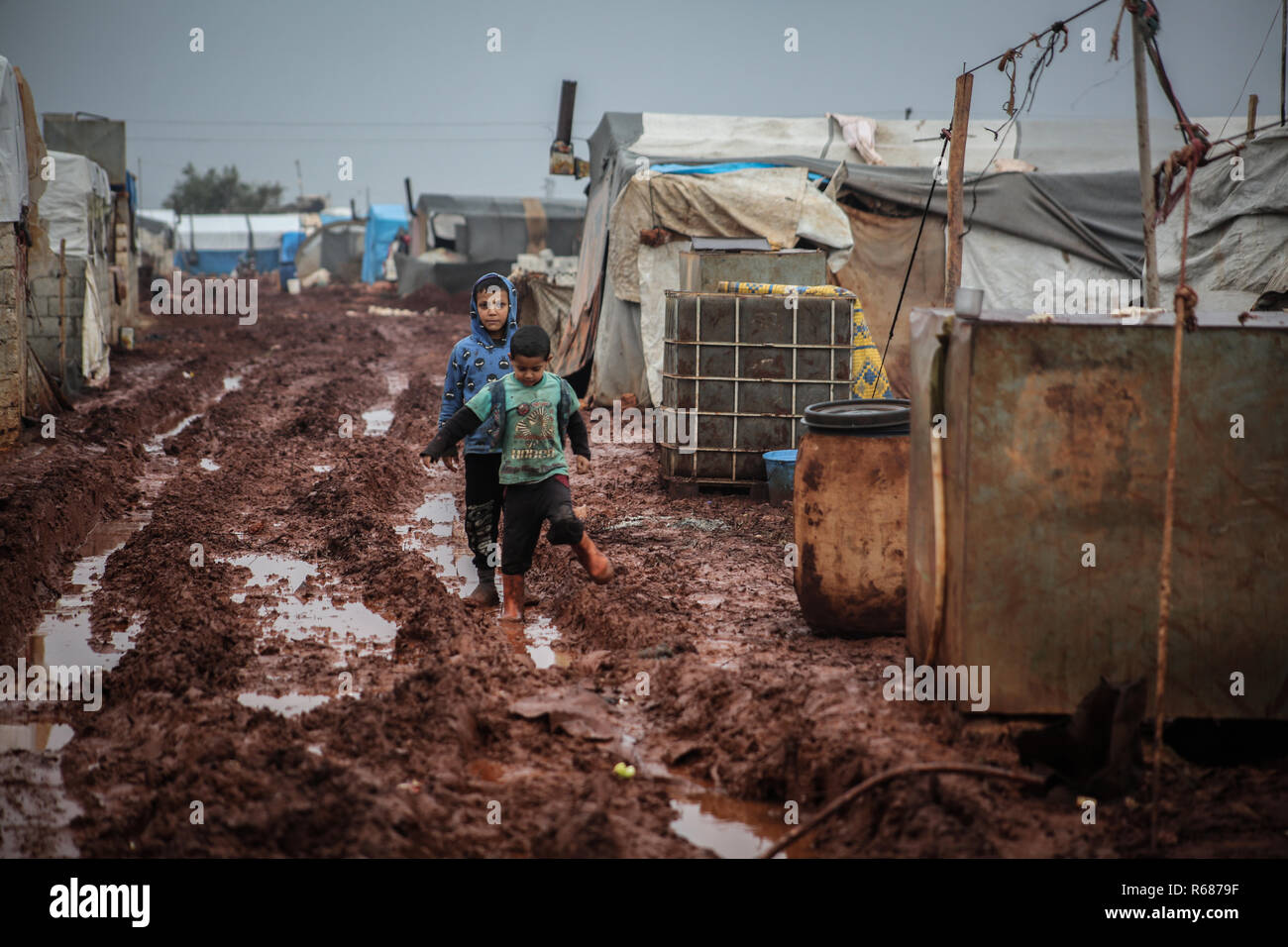 Idlib, Syrien. 04 Dez, 2018. Vertriebene Syrischen jungen Spaziergang durch den Schlamm bei Regenwetter an einem Lager für Vertriebene in der Nähe der syrischen Grenze Syrian-Turkish im nördlichen Umland von Idlib. Credit: Anas Alkharboutli/dpa/Alamy leben Nachrichten Stockfoto