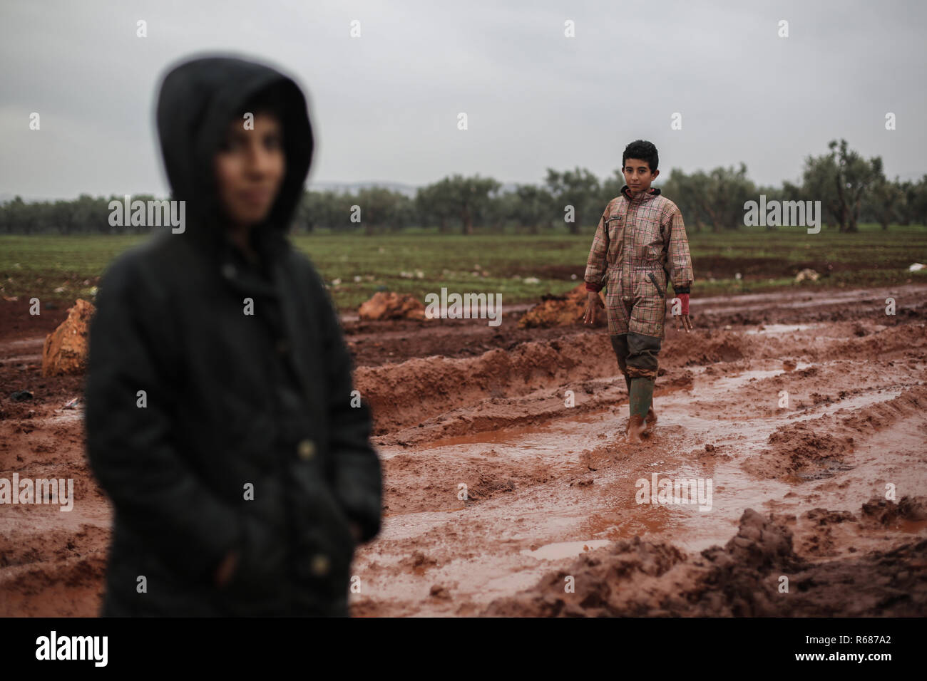 Idlib, Syrien. 04 Dez, 2018. Vertriebene Syrischen jungen Spaziergang durch den Schlamm bei Regenwetter an einem Lager für Vertriebene in der Nähe der syrischen Grenze Syrian-Turkish im nördlichen Umland von Idlib. Credit: Anas Alkharboutli/dpa/Alamy leben Nachrichten Stockfoto