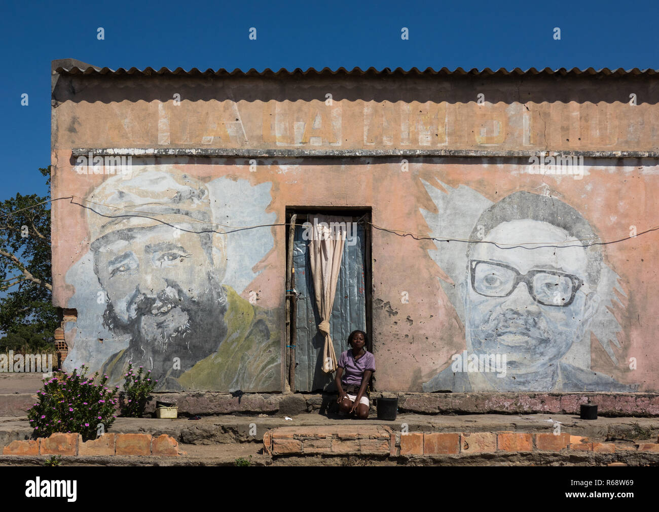 Junge Frau vor ihrem Haus mit einem alten kommunistischen Propaganda Wandmalerei von Fidel Castro und Agostinho Neto, Huila Provinz, Vilhambundu, Ango Stockfoto
