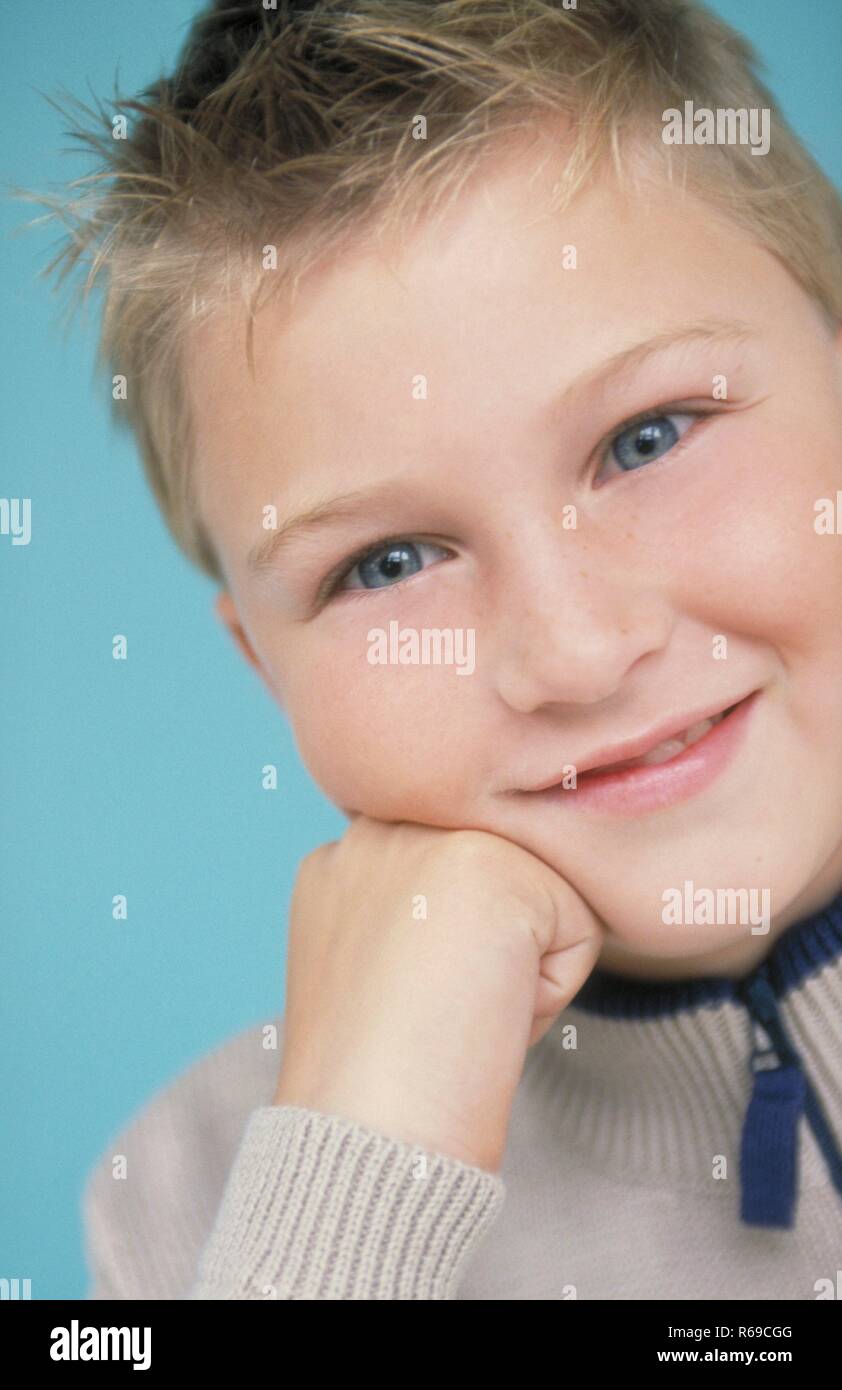 Porträt, Nahaufnahme, grinsender dunkelblondr Junge mit blauen Augen, 9 Jahre, Stuetzt sein Kinn in seine Hand Stockfoto