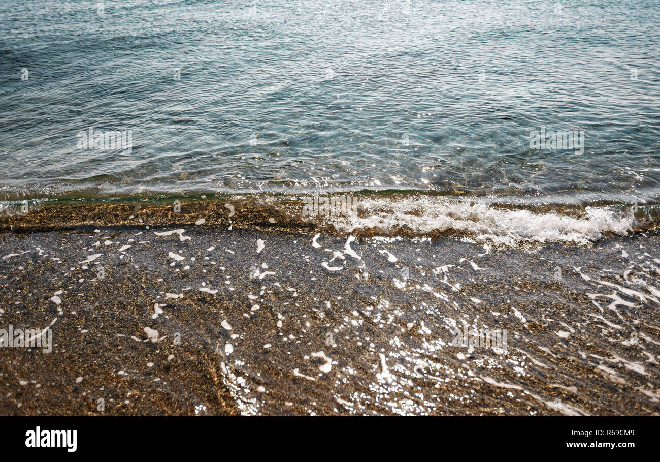 Nahaufnahme von einem kleinen klaren türkisblauen Meer Wasser Welle Abstürzen auf dem Sand. Stockfoto