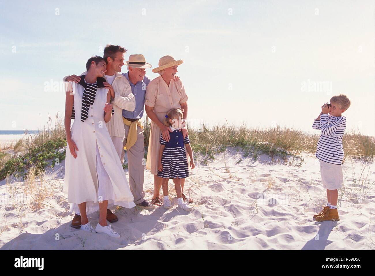 Strandszene, blonder Junge macht am Strand ein Gruppenfoto von ihrer Familie, mit den Eltern, Grosseltern und seiner kleinen Schwester Stockfoto