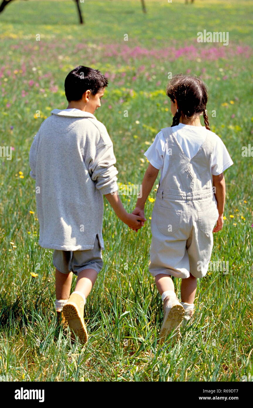 Outdoor, Jungen und Maedchen gehen Hand in Hand in einer Wiese mit wilden Blumen spazieren Stockfoto
