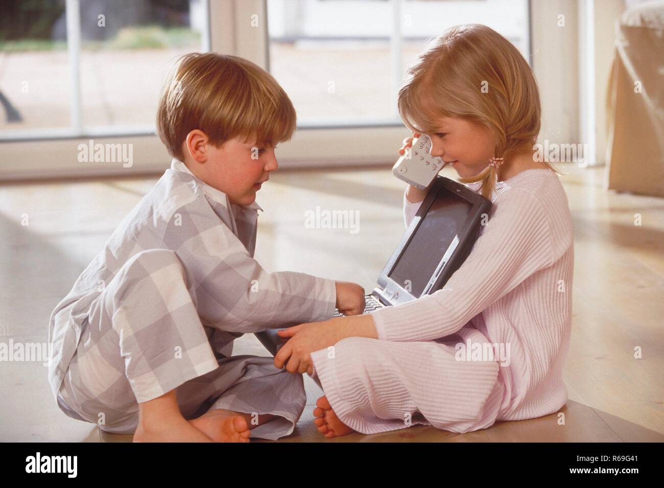 Innenraum, blonder Junge und Maedchen, 5-6 Jahre alt, bekleidet mit Nachthemd und Schlafanzug Artikel mit dem Holzboden und spielen am Laptop Stockfoto