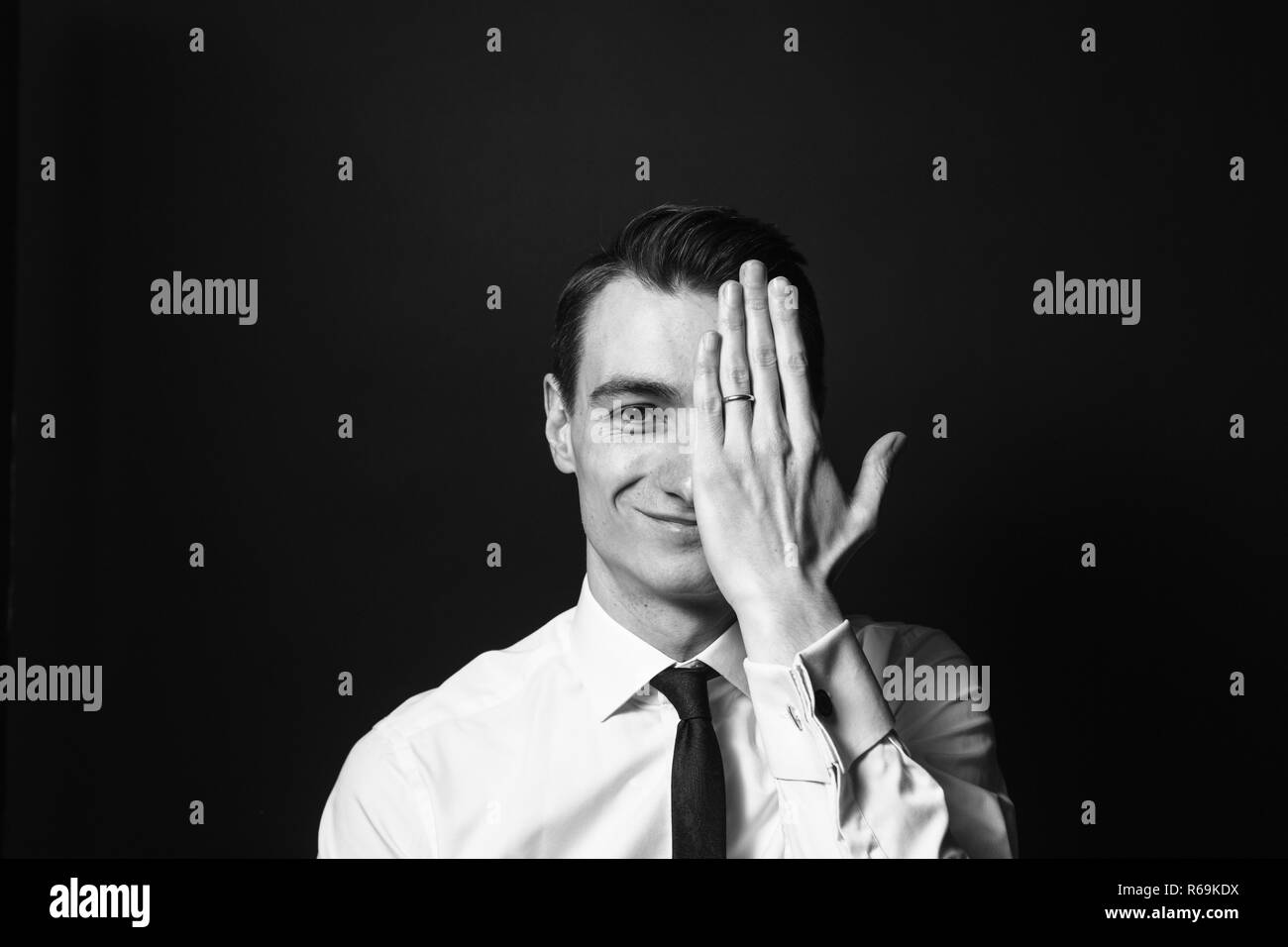 In der Nähe von Schwarzen und Weißen Porträt eines jungen Mannes in einem weißen Hemd und schwarzer Krawatte, Hand die halbe Gesicht in die Kamera schaut, gegen normales St Stockfoto