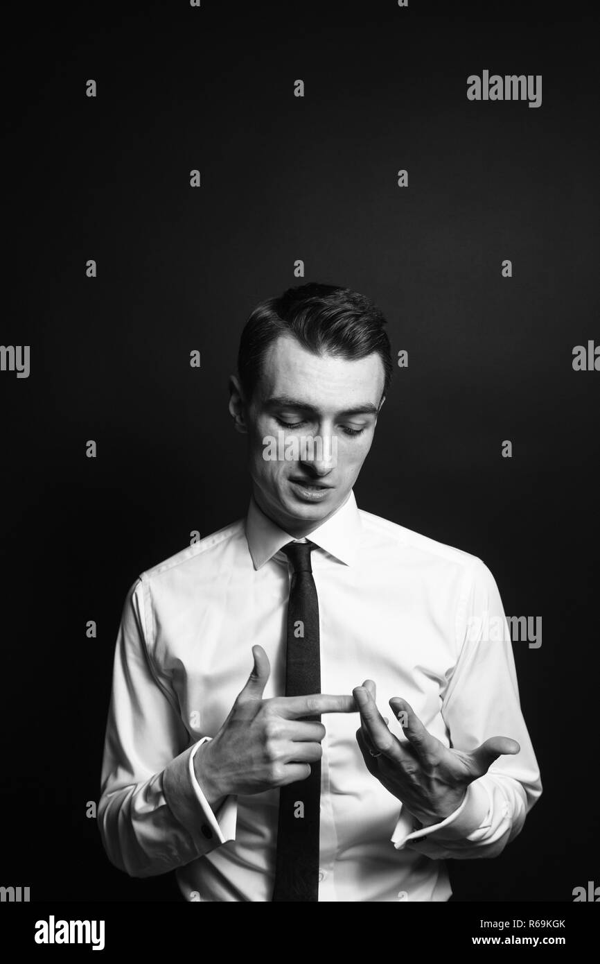In der Nähe von Schwarzen und Weißen Porträt eines jungen Mannes in einem weißen Hemd und schwarzer Krawatte, zählen mit den Fingern und sprechen, auf einen einfachen Studio backgro Stockfoto