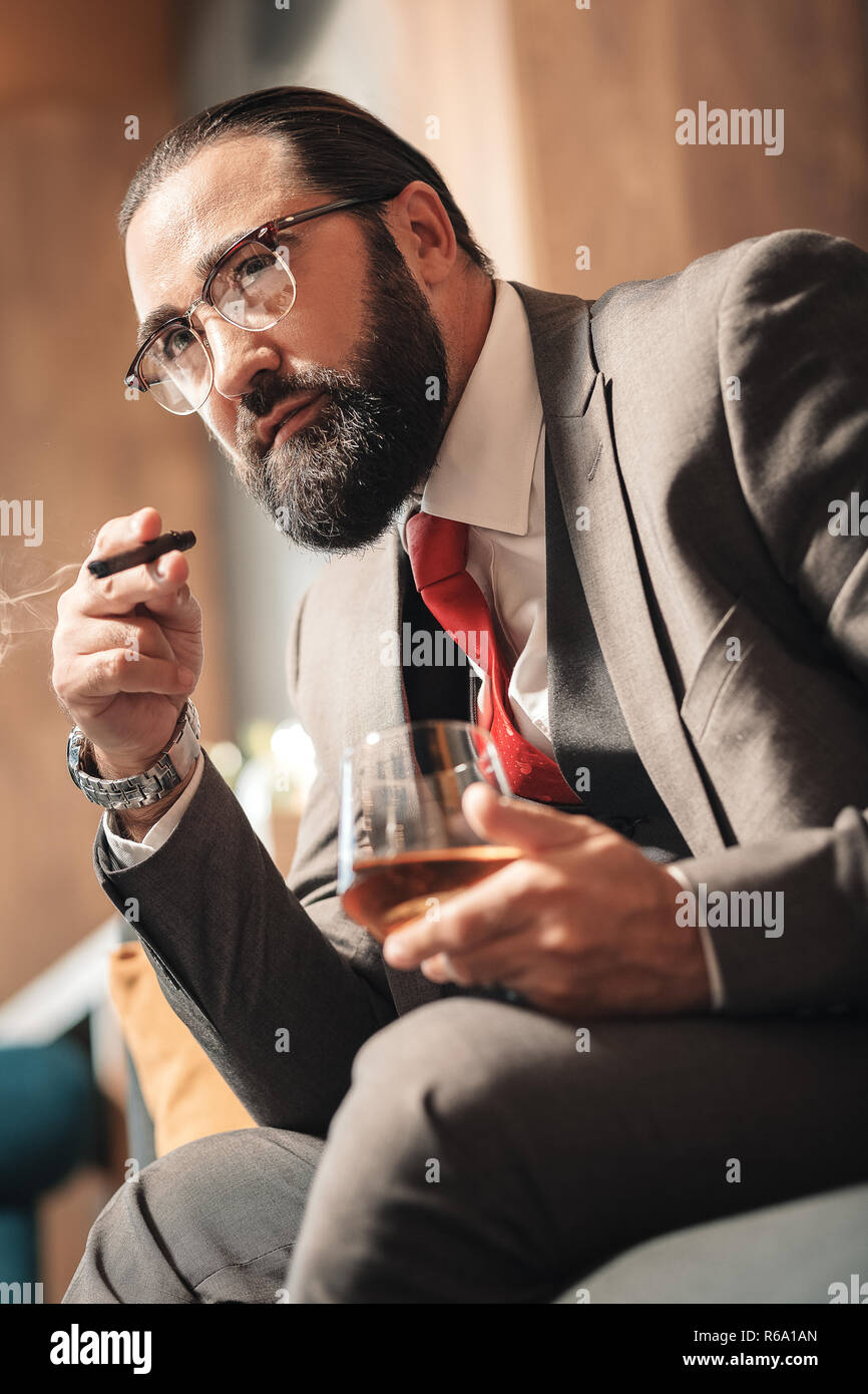 Bärtige Geschäftsmann sitzen in bequemen Sessel rauchen und trinken Stockfoto
