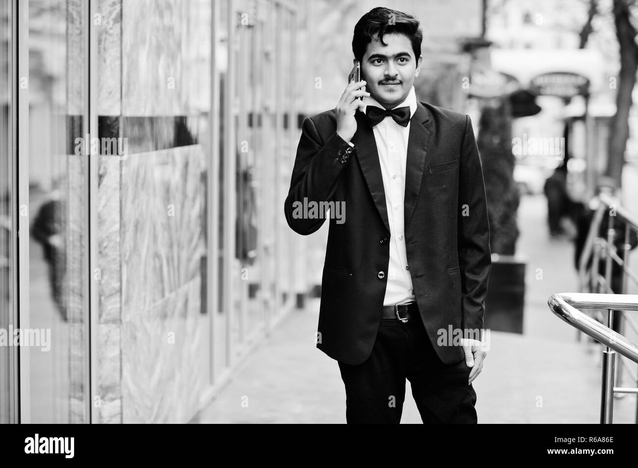 Junge Inder auf schwarzen Anzug und Fliege outdoor gestellt, sprechen am Telefon. Stockfoto