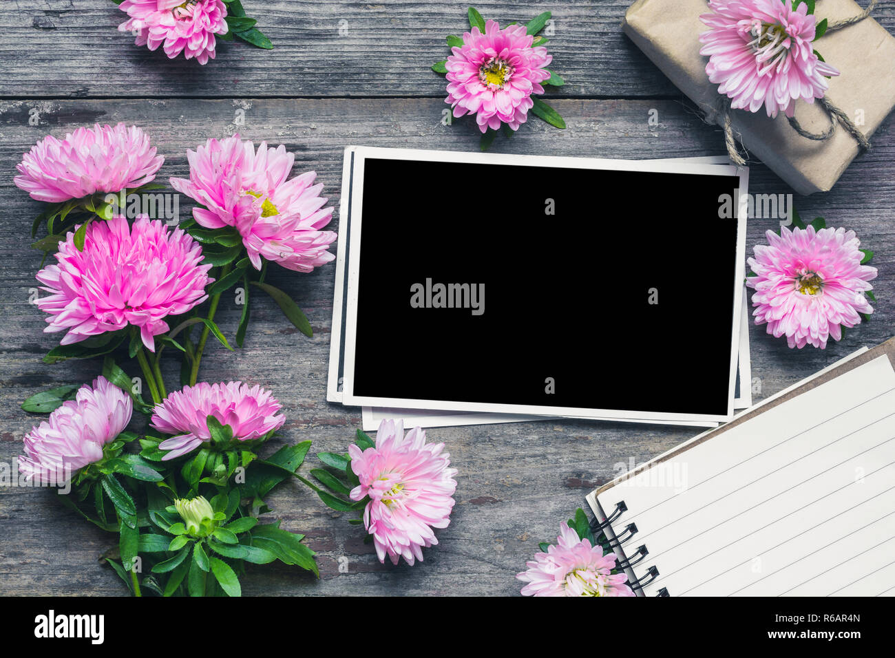 Leeren Bilderrahmen mit schönen Blumenstrauß rosa aster Blumen, Notepad und Geschenkbox. Mock up.Layout.flatlay. Urlaub oder Hochzeit Hintergrund. nach oben vie Stockfoto