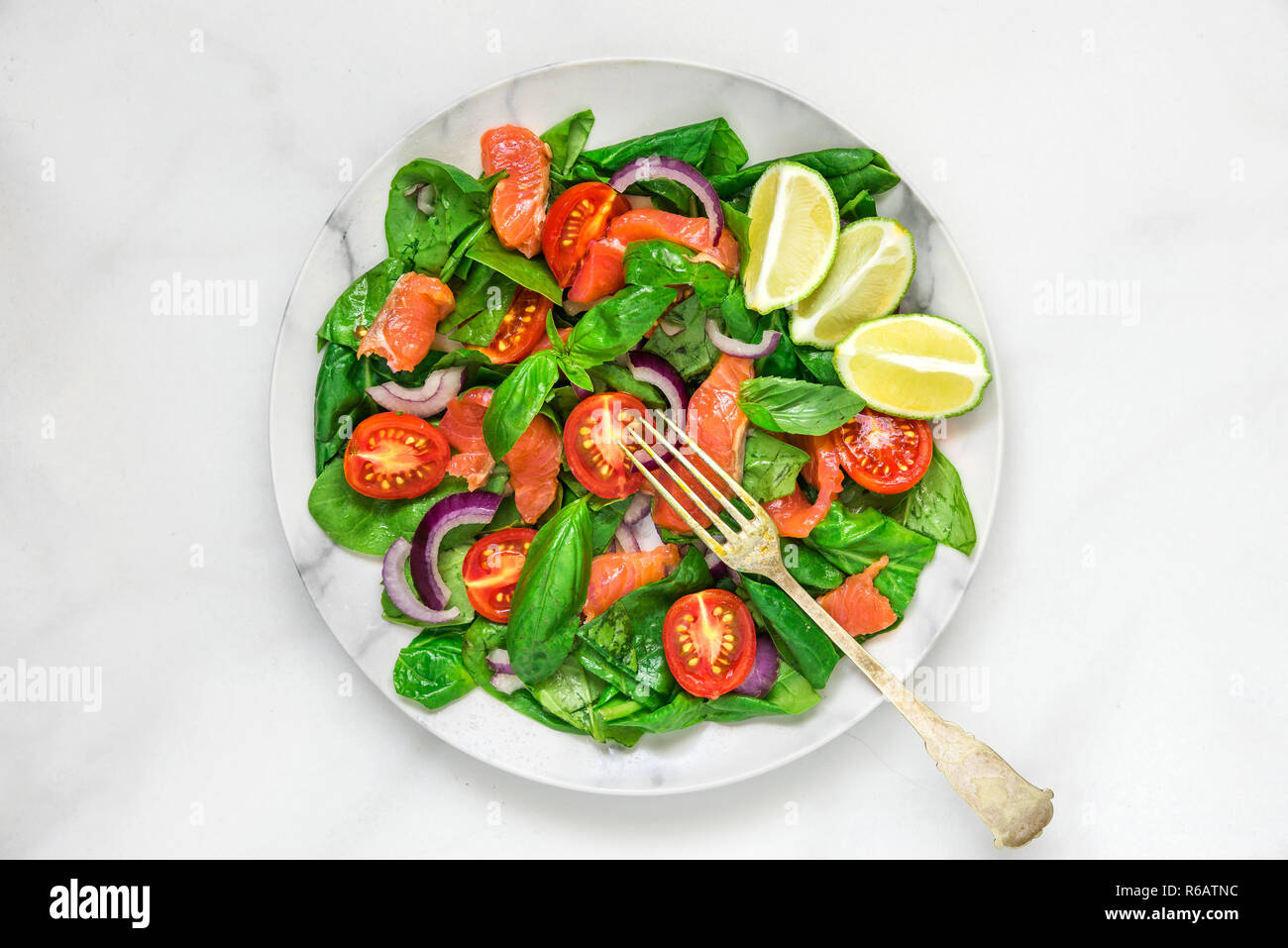 Lachs Salat mit Spinat, Tomaten, roten Zwiebeln, Zitrone und Basilikum in einen Teller mit Gabel auf weißem Hintergrund. gesunde Ernährung Konzept. nach oben vi. Stockfoto
