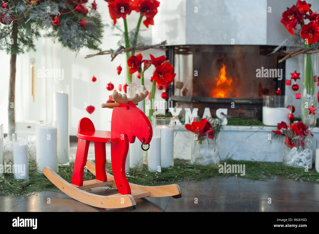 Kamin Einrichtung mit Kerzen und roten Blüten. Schaukelstuhl. Stockfoto