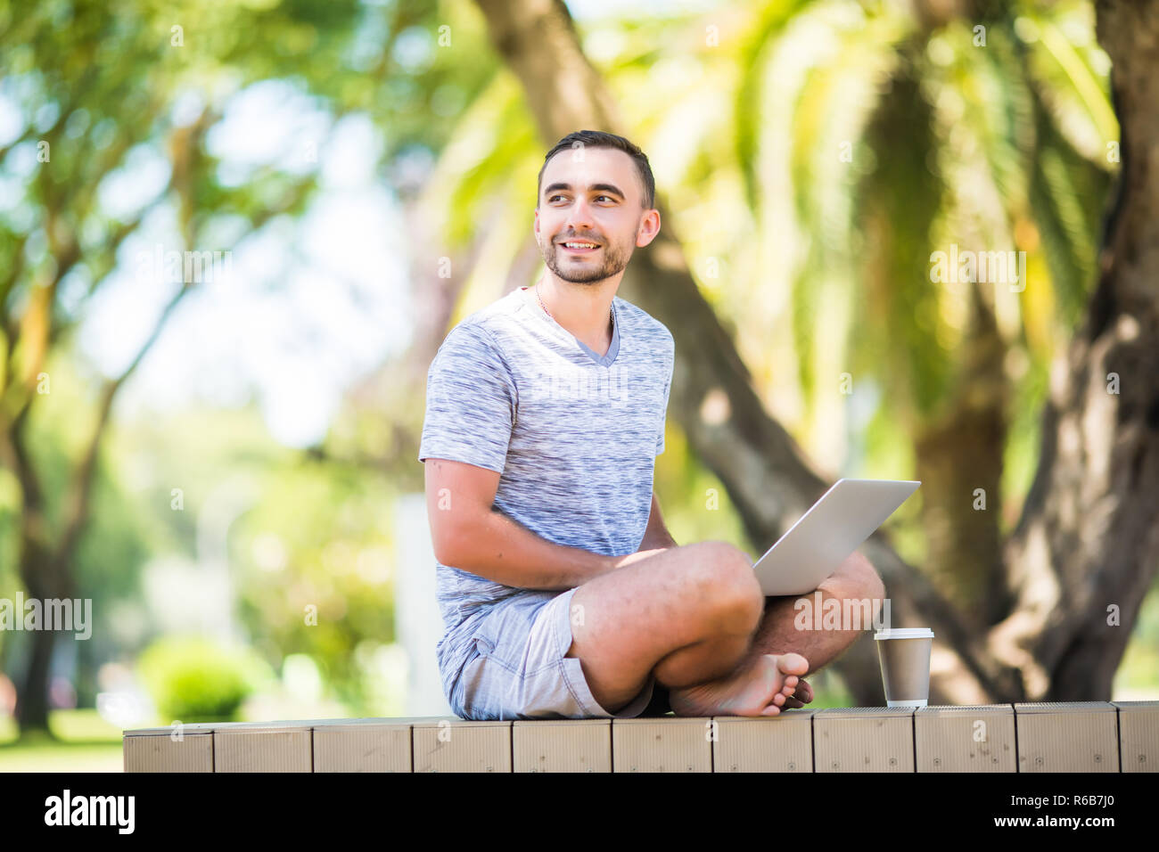 Junger Mann mit Laptop sitzt auf einer Holzbank Stockfoto
