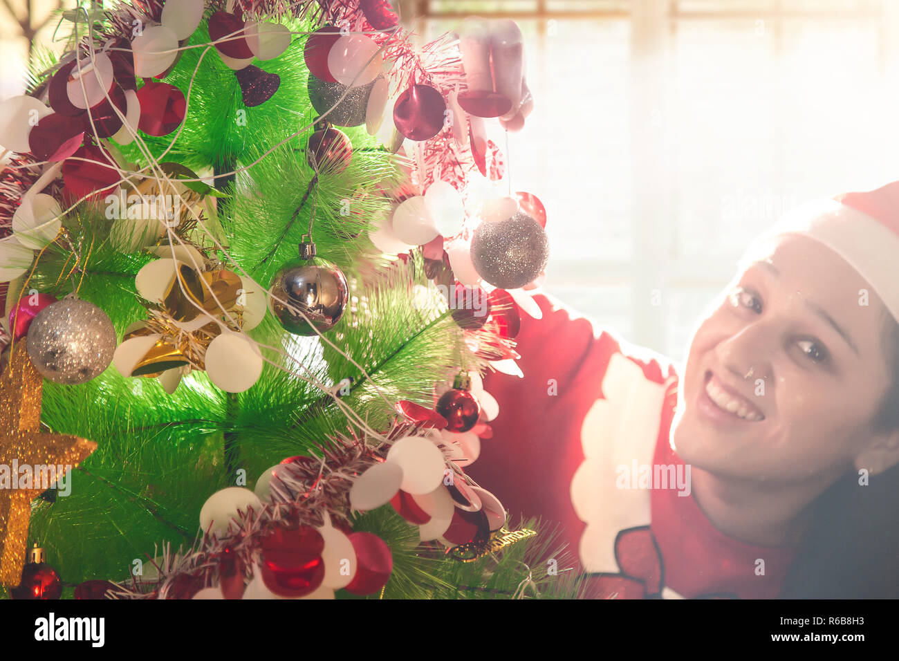 Schöne junge Frau in Santa Hut schmücken Weihnachtsbaum zu Hause Stockfoto