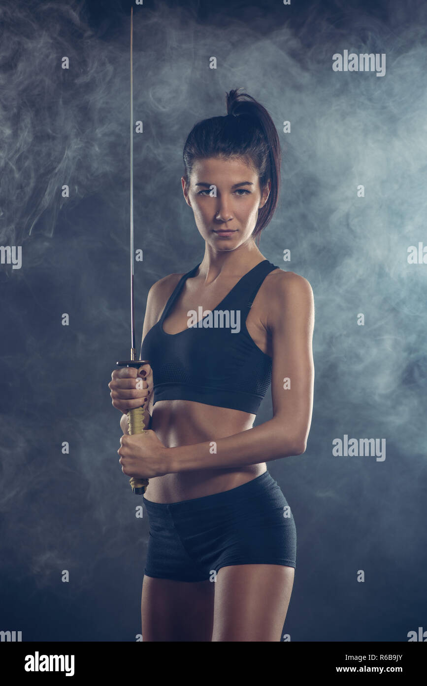 Porträt einer wunderschönen jungen Frau mit dem Schwert und mit einem ernsten Gesichtsausdruck in die Kamera schaut. Der dunkle Hintergrund. Stockfoto