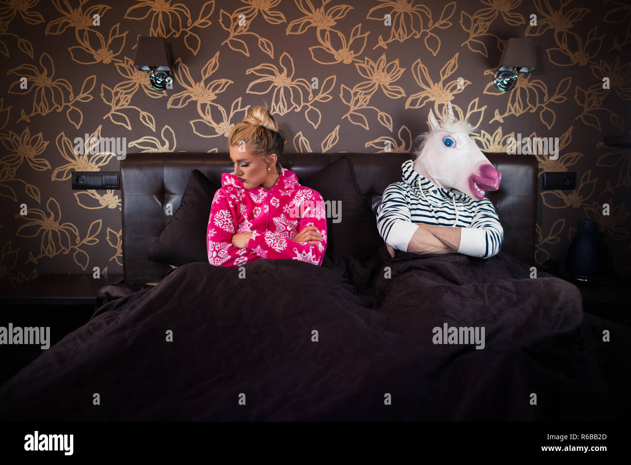 Ungewöhnliche Paar hat Beziehung Probleme. Schöne junge Frau im Pyjama auf dem Bett mit seltsamen Freund in freaky Maske in stilvoll eingerichteten Apartments. Stockfoto