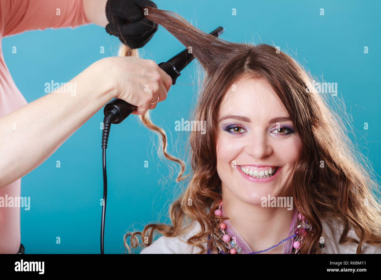 Friseur curling Frau Haar mit elektrischen Eisen Lockenstab Tong. Hairstylist machen Mädchen Frisur. Attraktive hübsche junge Frau. Schönheit. Stockfoto