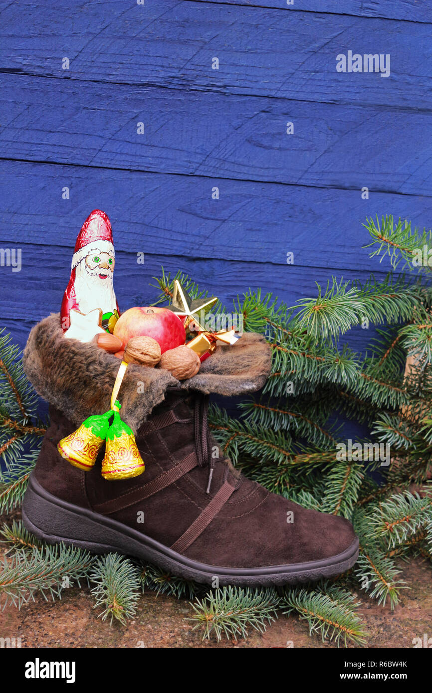 Weihnachtsstrumpf mit Schokolade Nikolaus oder Weihnachtsmann, Apple und Muttern vor einem blauen Hintergrund aus Holz Stockfoto