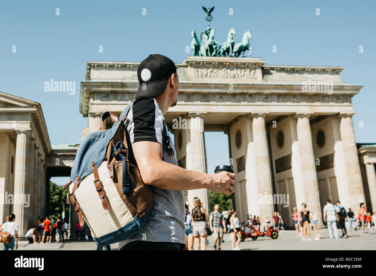 Eine Person hält eine Tasse mit Kaffee oder einem anderen Getränk beim Gehen oder Sightseeing in Berlin, Deutschland. Vor dem Brandenburger Tor und verschwommen, unbekannte Menschen. Stockfoto