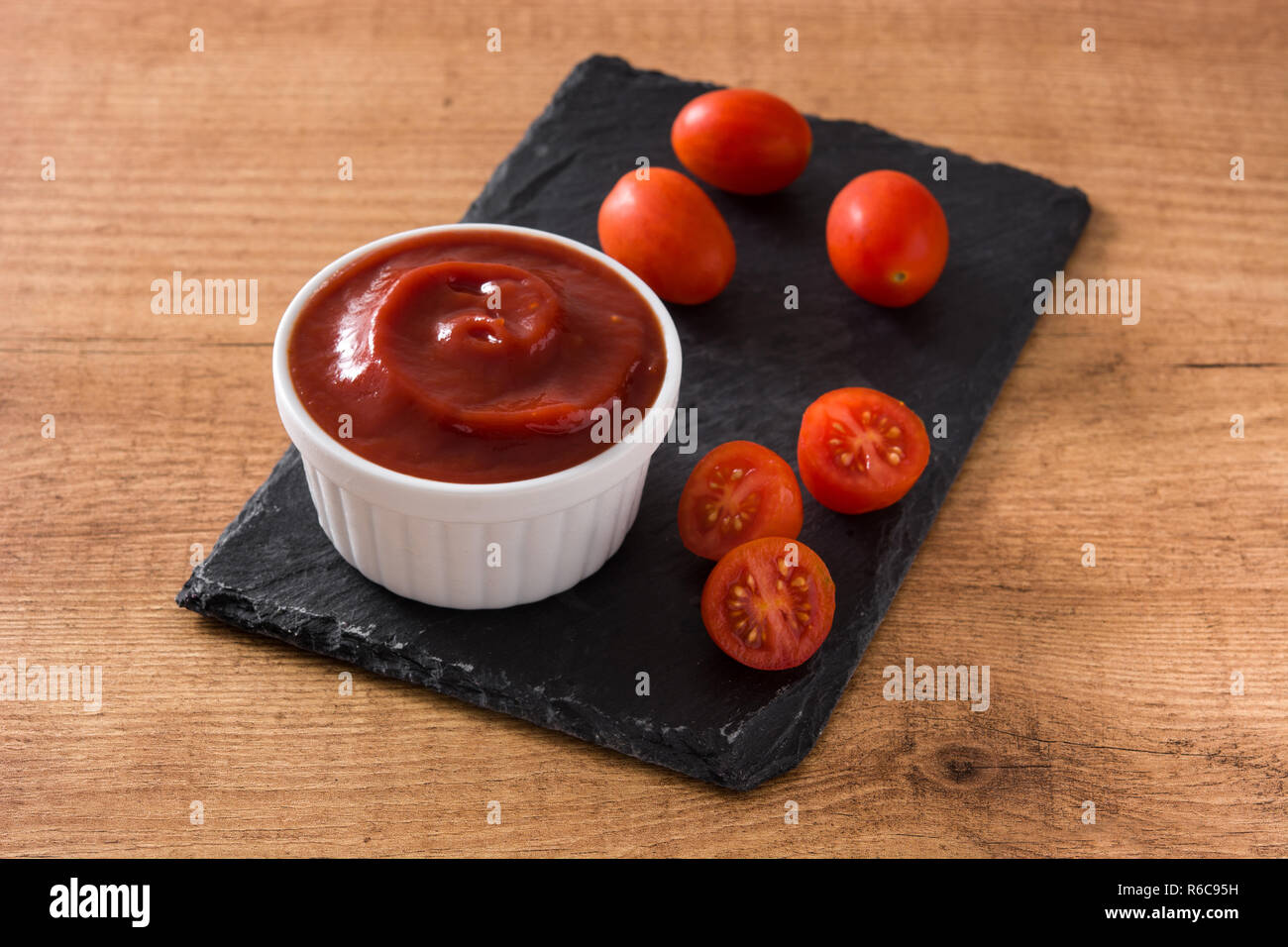 Ketchup Sauce in der Schüssel und Tomaten auf hölzernen Tisch Stockfoto