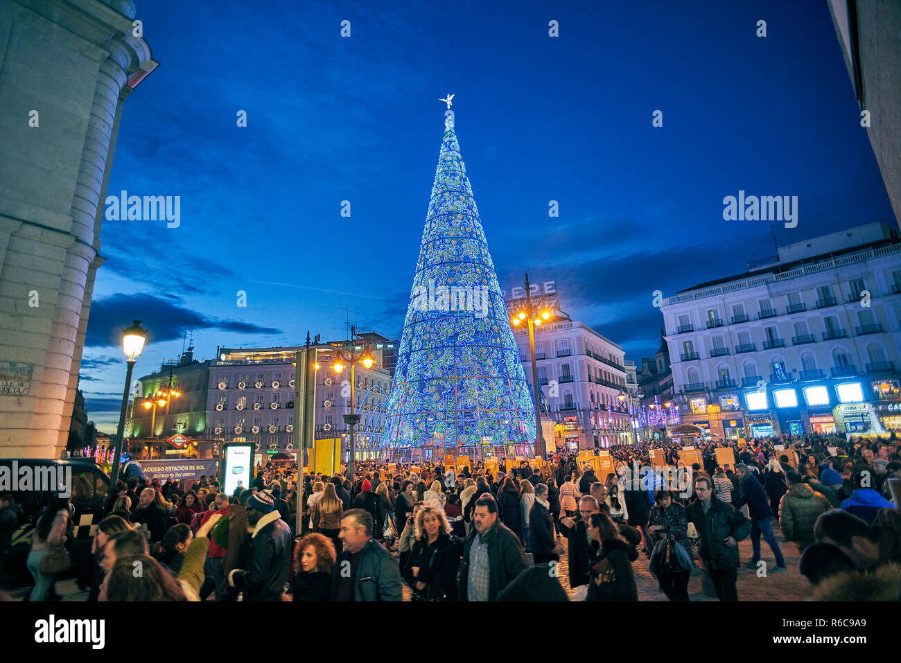 Puerta del Sol Platz bei Einbruch der Dunkelheit durch die Weihnachtsbeleuchtung und ein glänzender Weihnachtsbaum beleuchtet. Blick von der Calle de Carretas Straße. Stockfoto