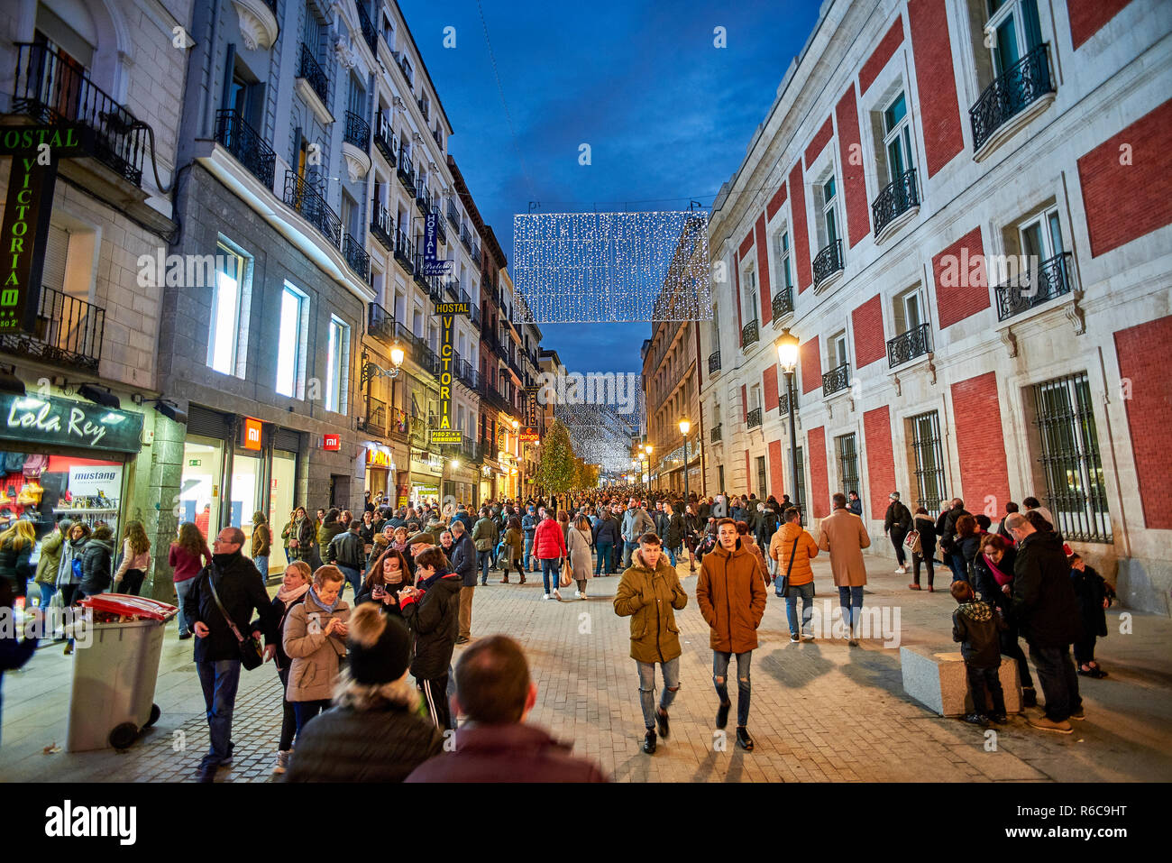 Menschen zu Fuß auf die Calle Carretas Straße bei Einbruch der Dunkelheit durch die Weihnachtsbeleuchtung illuminiert. Blick von der Puerta del Sol. Stockfoto