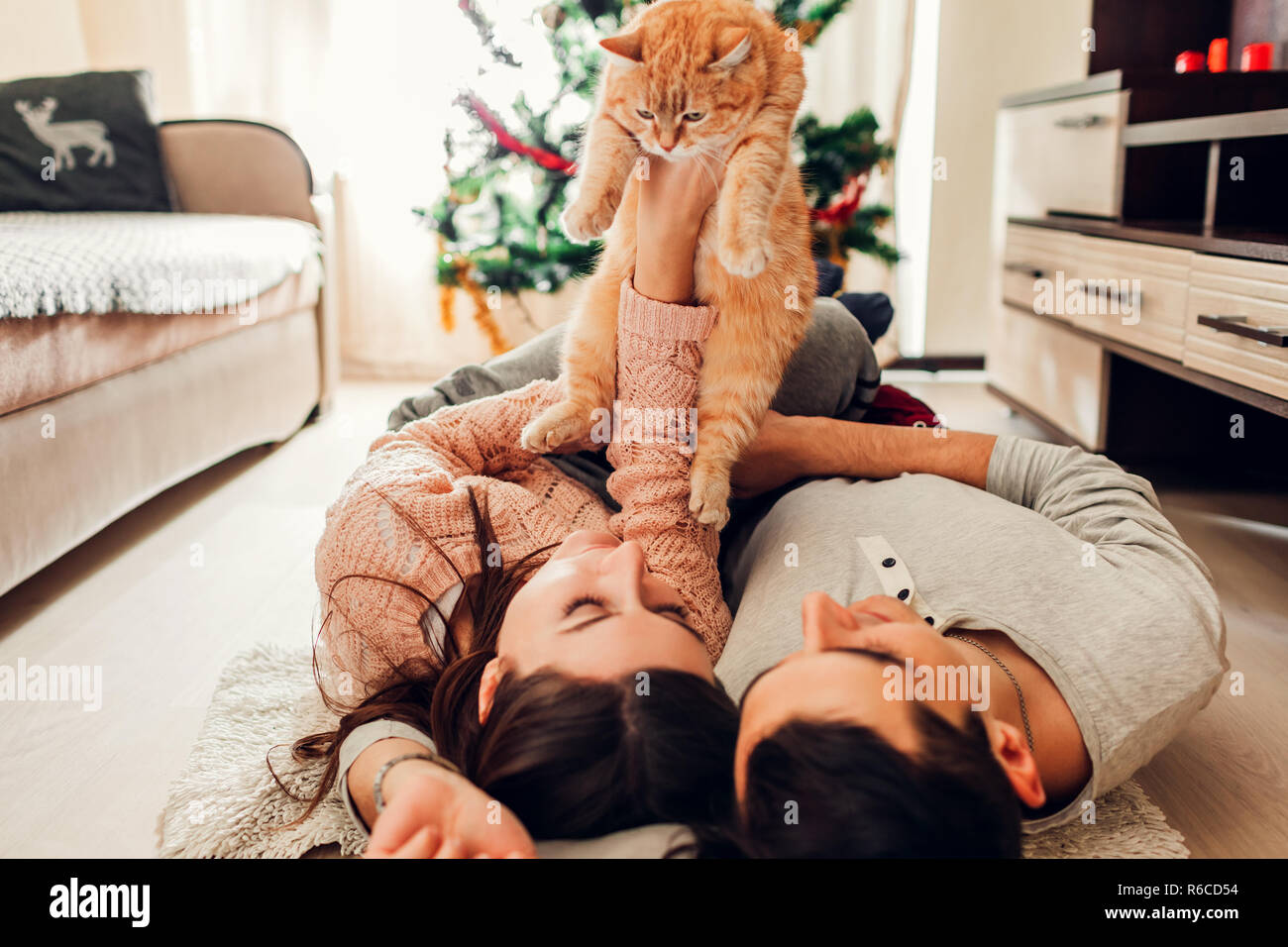 Verliebtes Paar liegen, Weihnachtsbaum und das Spielen mit der Katze zu Hause. Mann und Frau Heben von Pet in den Händen. Glückliche Familie Stockfoto