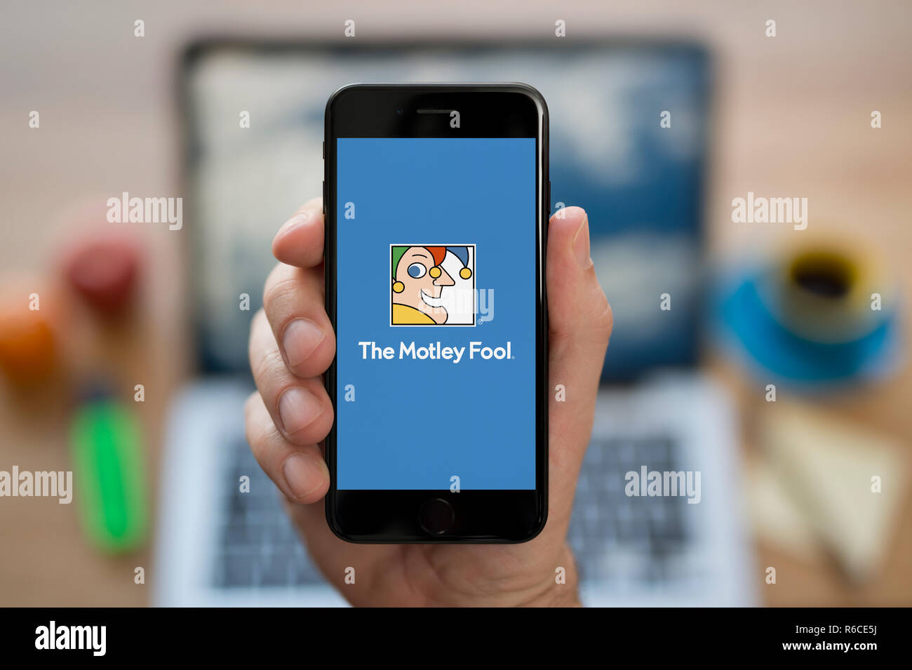 Ein Mann schaut auf seinem iPhone. Das Motley Dummkopf logo, während saß an seinem Computer Schreibtisch (nur redaktionelle Nutzung). Stockfoto