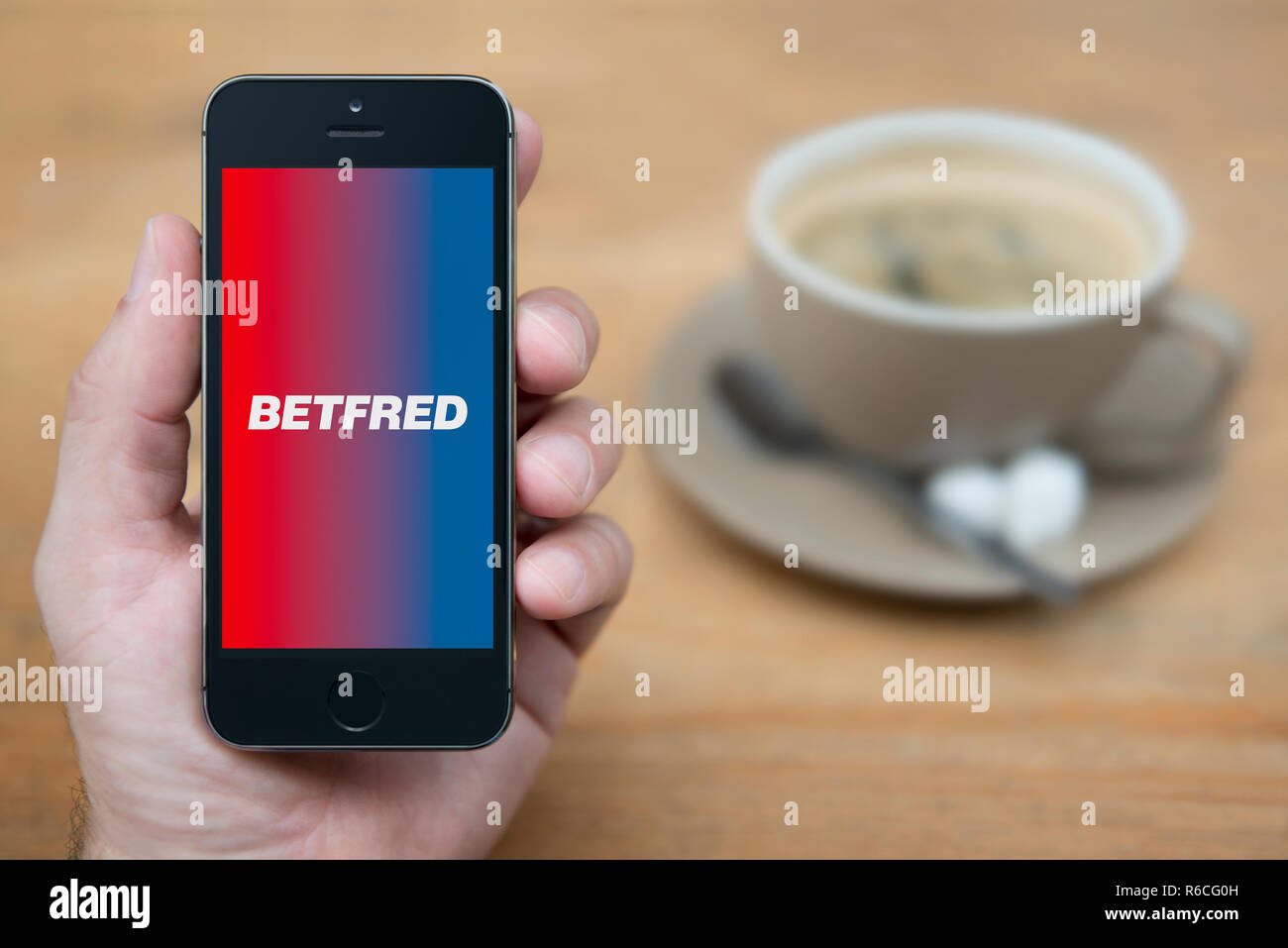 Ein Mann schaut auf seinem iPhone die zeigt die Betfred Logo (nur redaktionelle Nutzung). Stockfoto