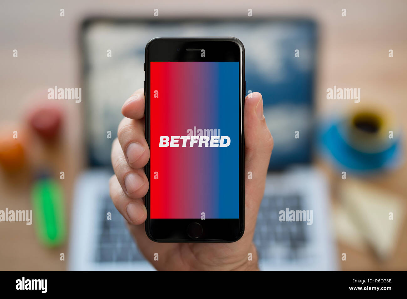 Ein Mann schaut auf seinem iPhone die zeigt die Betfred logo, während saß an seinem Computer Schreibtisch (nur redaktionelle Nutzung). Stockfoto