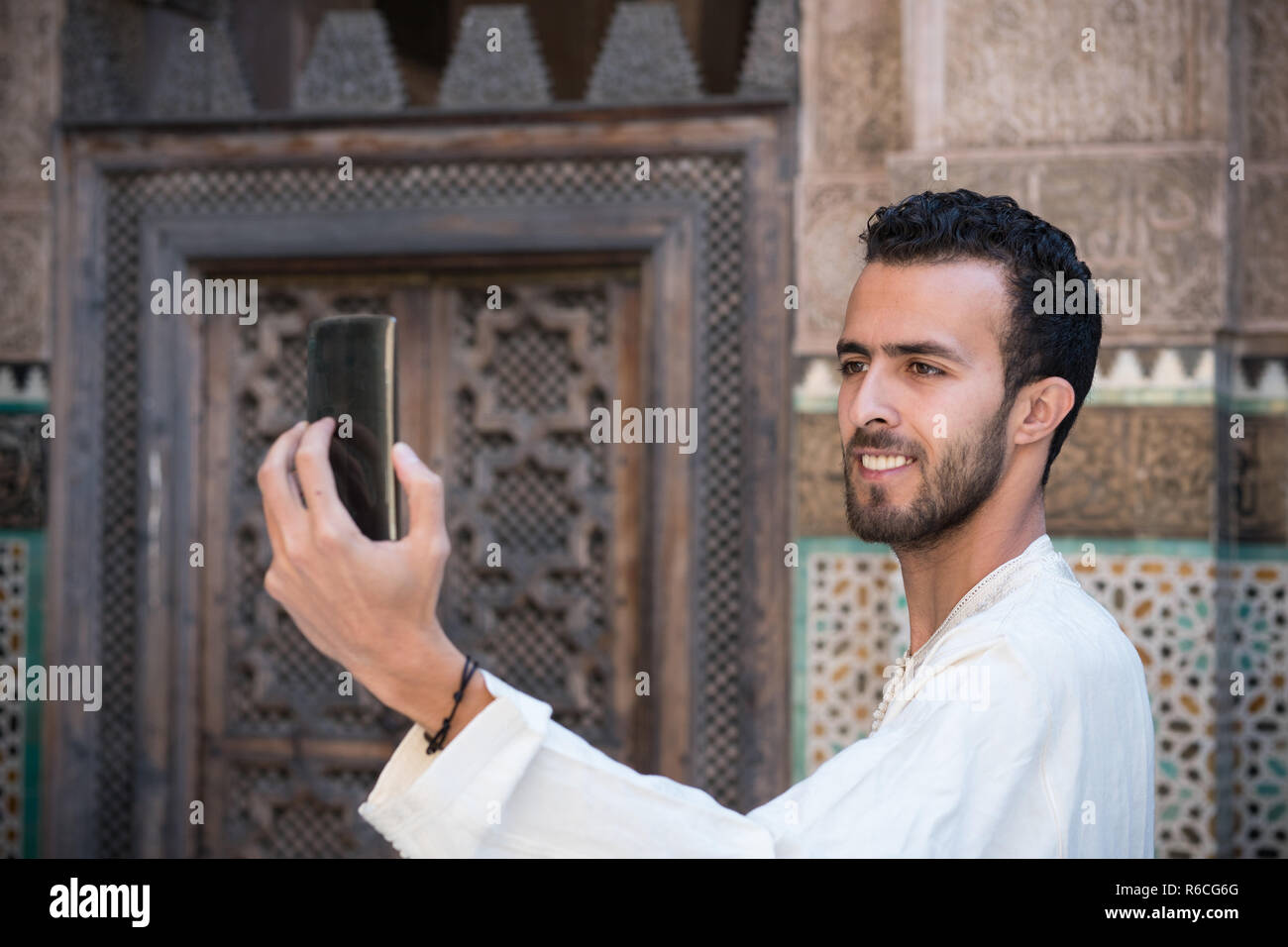 Junge muslimische Mann in traditioneller Kleidung lächelnd und unter selfie mit Handy Stockfoto