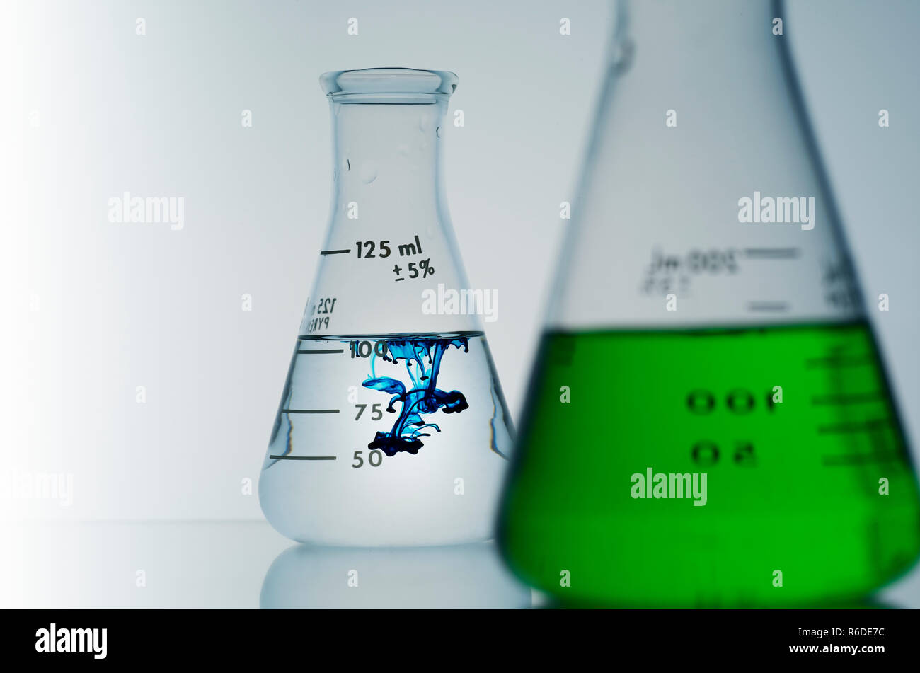 Zwei konische Kolben mit grünen und blauen Flüssigkeiten, Fokus auf Hintergrund. Stockfoto