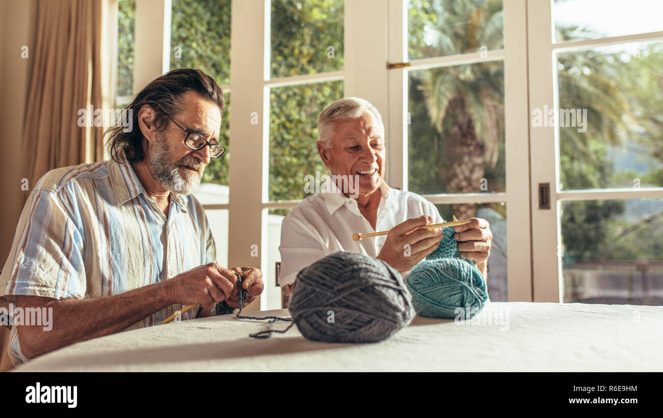 Alte Männer zu Hause sitzen und Stricken Pullover mit den Stricknadeln und Wollfäden. Ältere Menschen lernen Stricken an pensionierte Alter. Stockfoto