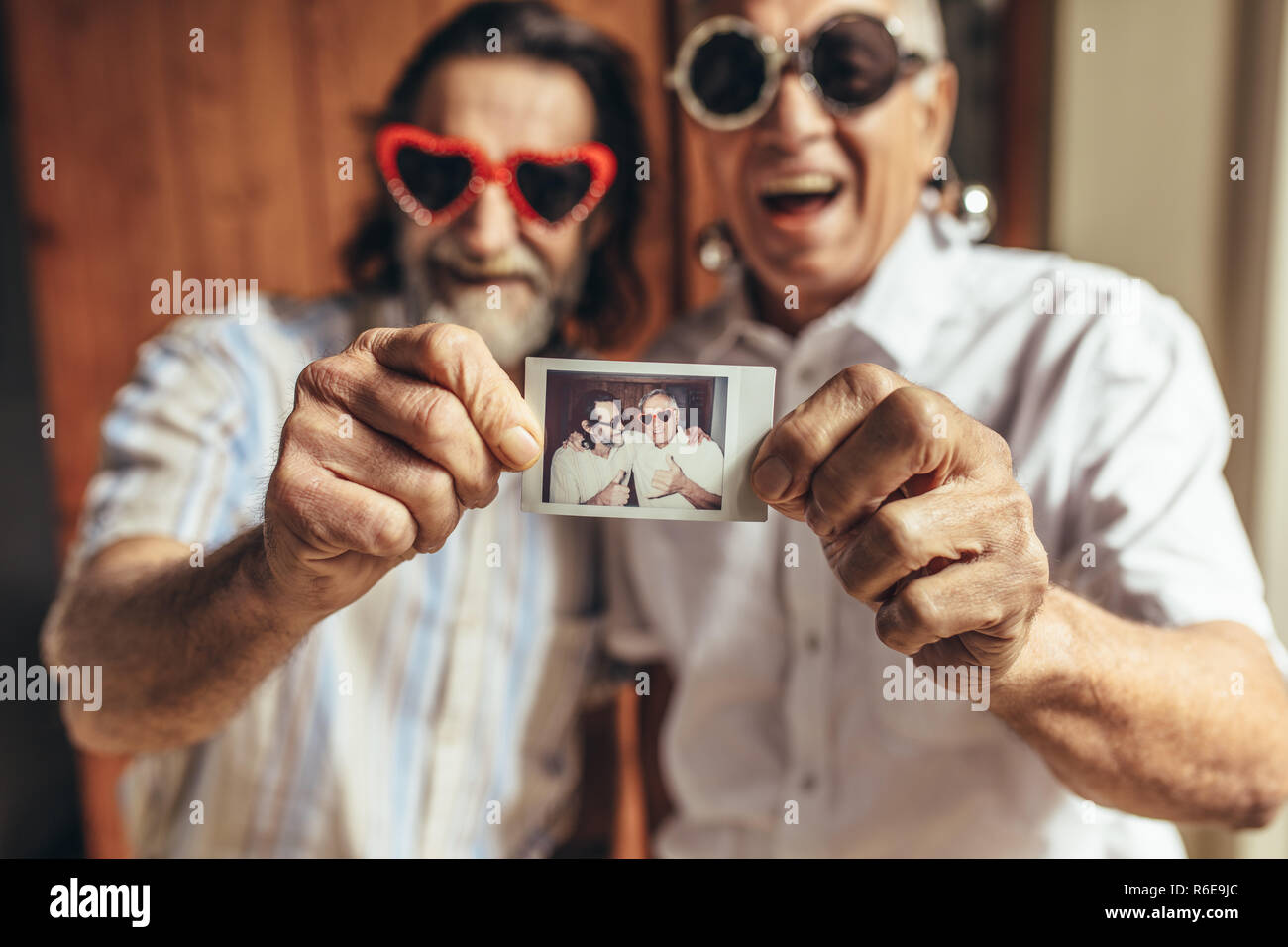 Zwei ältere männliche Freunde mit Party Sonnenbrille ihr Bild angezeigt. Ältere Menschen, die tolle Zeit zusammen. Fokus auf das Bild in der Hand der alten Menschen Stockfoto