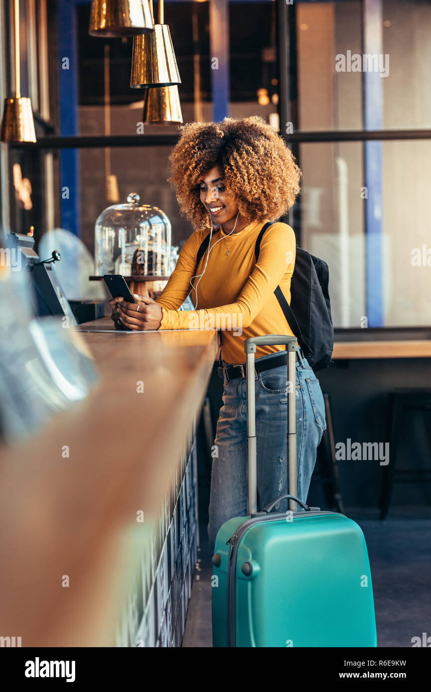 Weibliche Reisende stehen in einem Restaurant mit ihrem Gepäck Tasche auf Ihr Mobiltelefon. Afro-amerikanischer Tourist Frau, die auf der Abrechnung counte Stockfoto