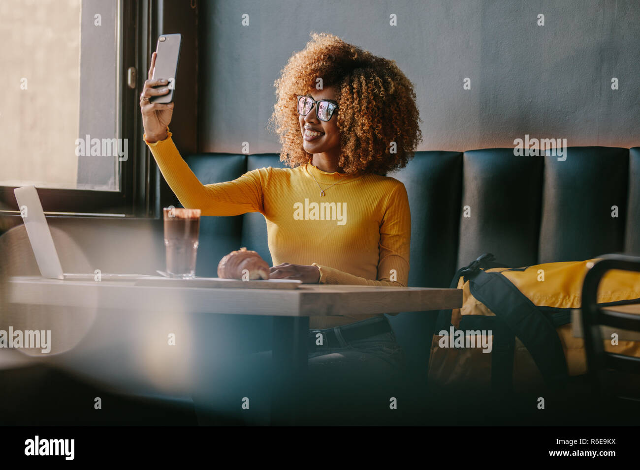 Lächelnd afro-amerikanische Frau die selfie auf Handy in einem Restaurant mit Snacks und Laptop auf dem Tisch sitzen. Weibliche Touristen speisen in einem Restaurant Stockfoto