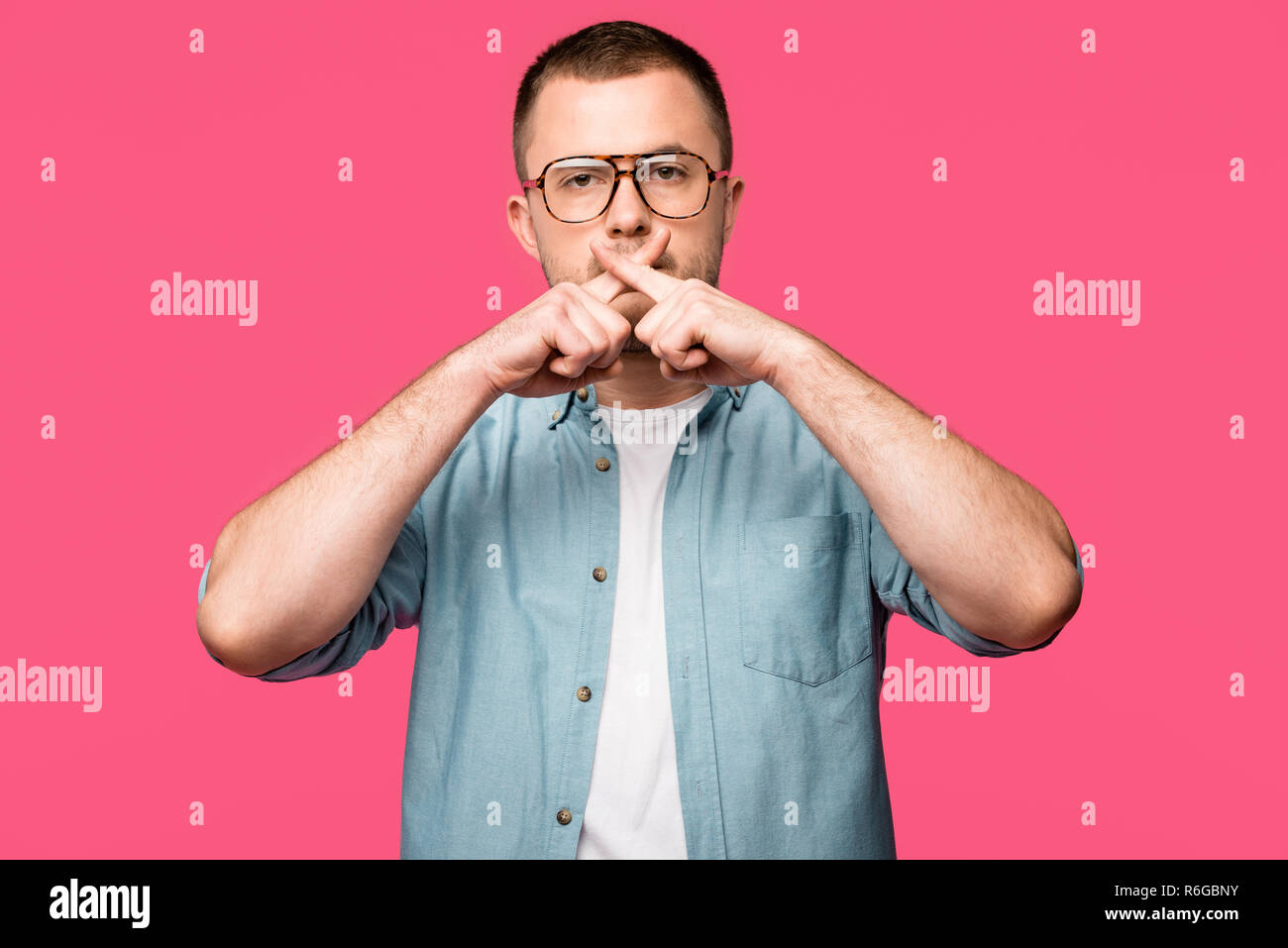 Junger Mann in Brillen Gestik für Stille und mit gekreuzten Fingern in der Nähe von Lippen isoliert auf Rosa Stockfoto