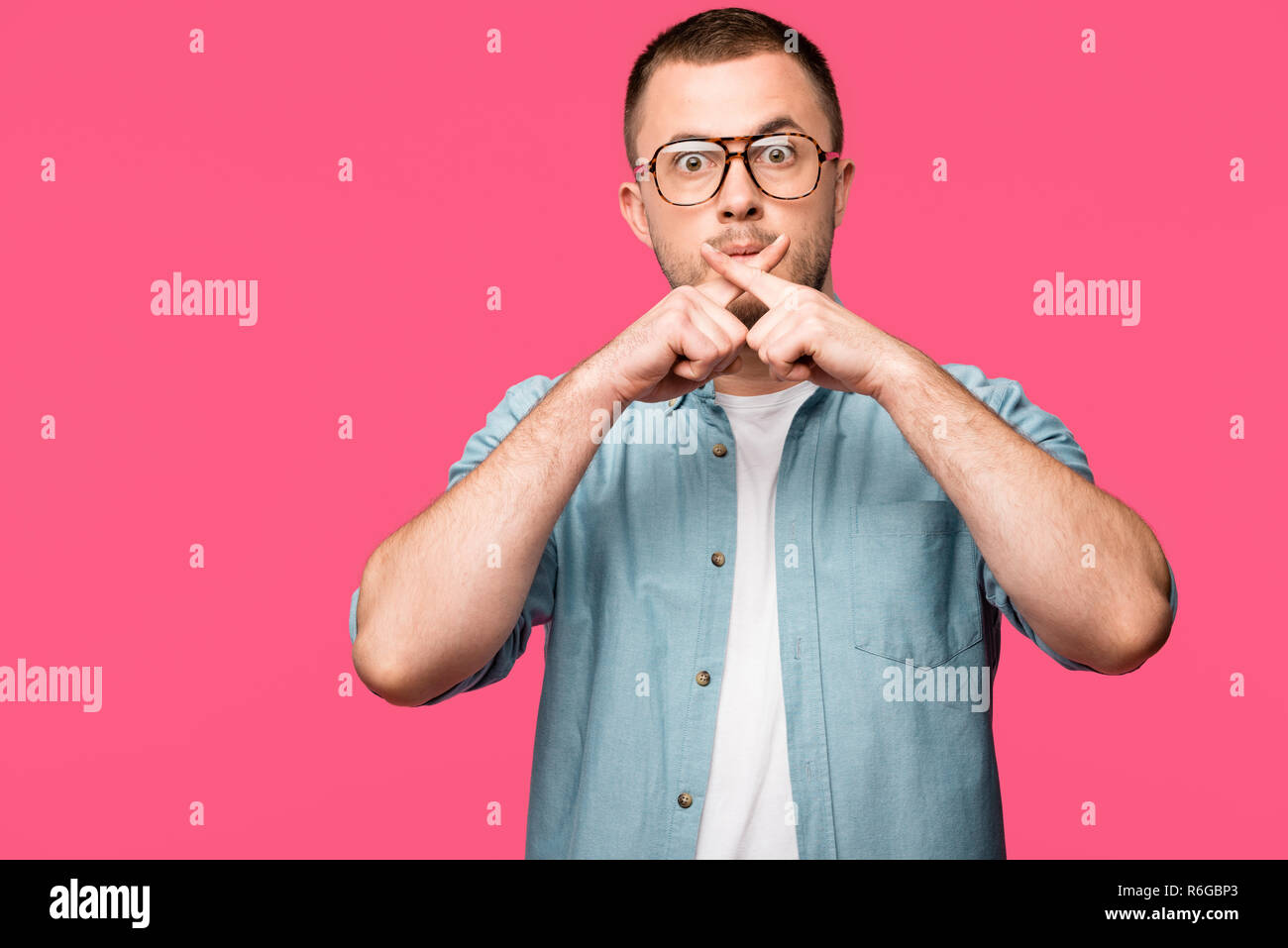 Junger Mann Gestik für Stille und die Finger in die Nähe von Lippen isoliert auf Rosa gekreuzt schockiert Stockfoto